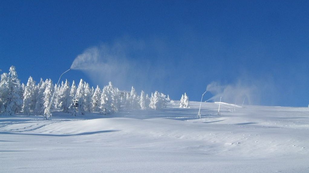 Beschneiung - Symbolbild eines beschneiten Pistenhangs, blauer Himmel.